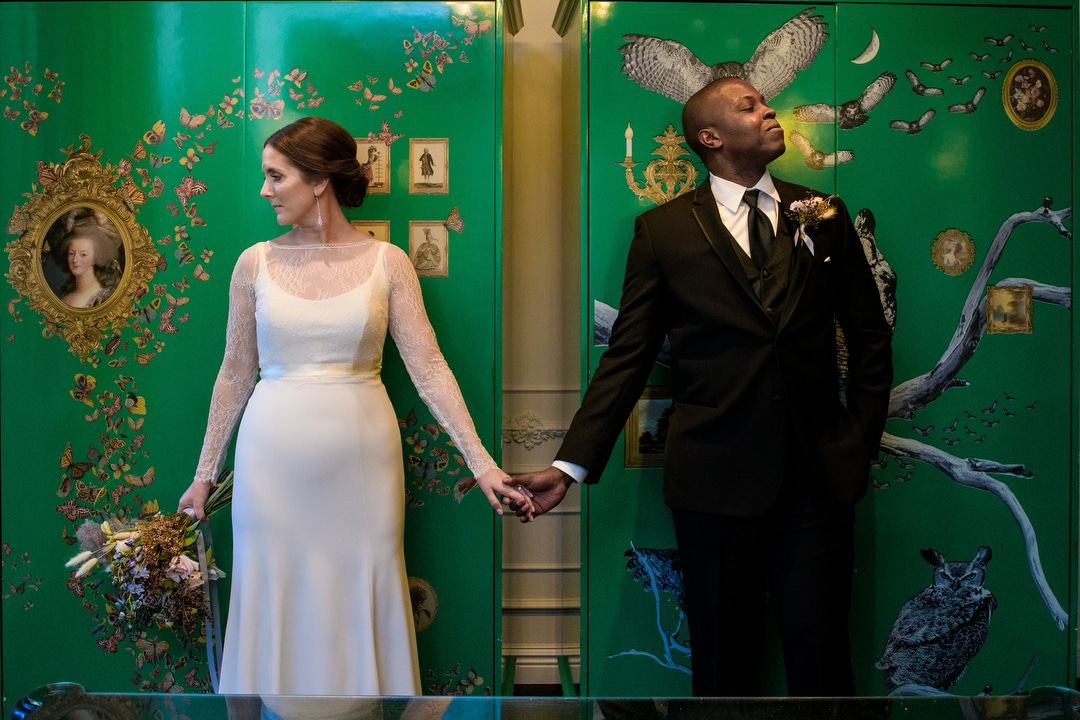A bride and groom hold hands in front of a green lacquer cabinet at the Hotel Monaco Pittsburgh before their wedding.