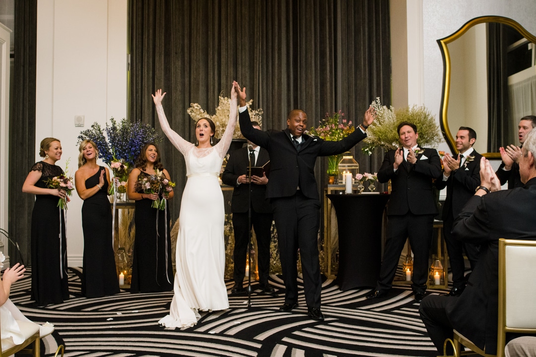 A bride and groom raise their hands in celebration at the end of their wedding ceremony at the Hotel Monaco Pittsburgh.