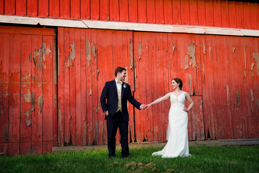 A bride and groom hold hands as they stand in front of the red barn at Gilfillan Farm in Upper St. Clair.