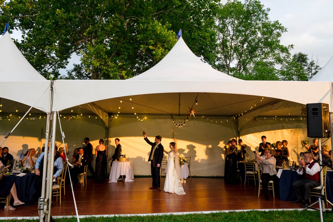 A bride and groom wave to their guests as they're introduced into their tented wedding reception.