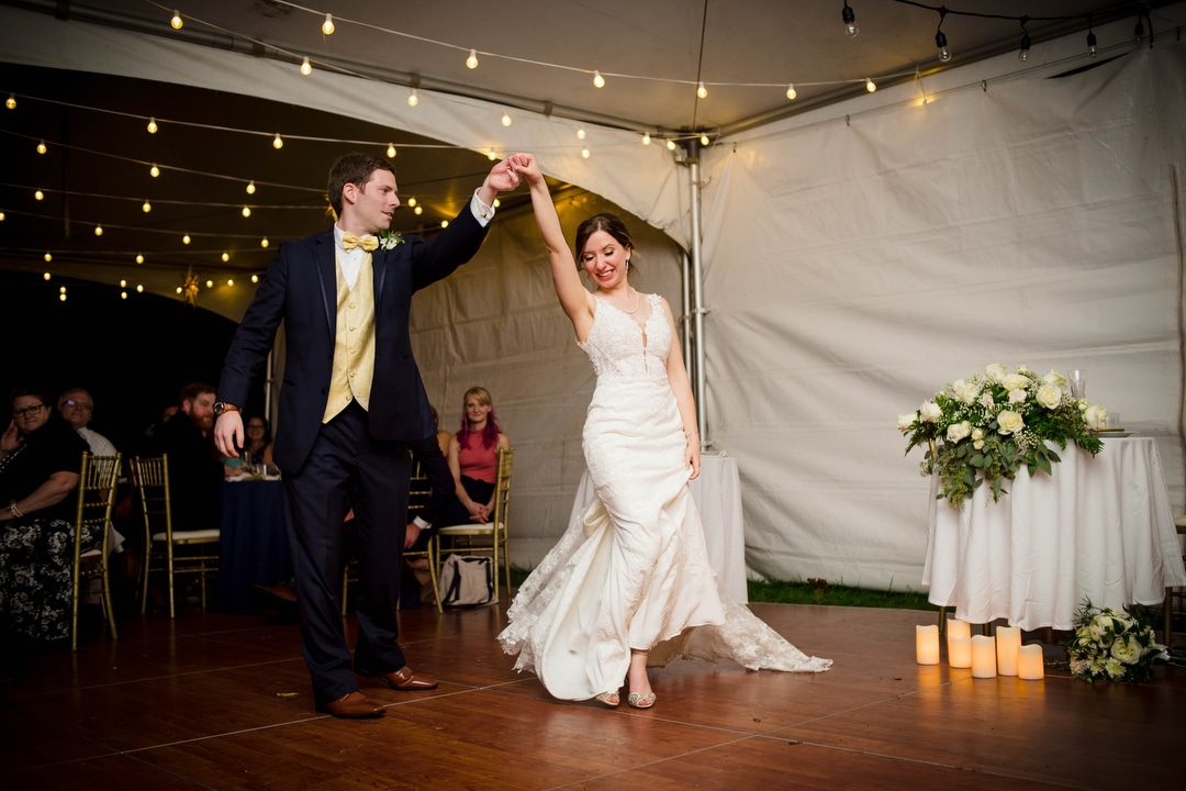 A bride and groom share a first dance with a tented reception with bistro lights hung above them.