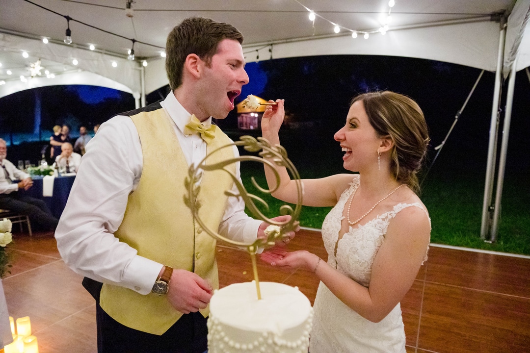 A bride feeds her groom a piece of wedding cake during their tented reception at Gilfillan Farm.