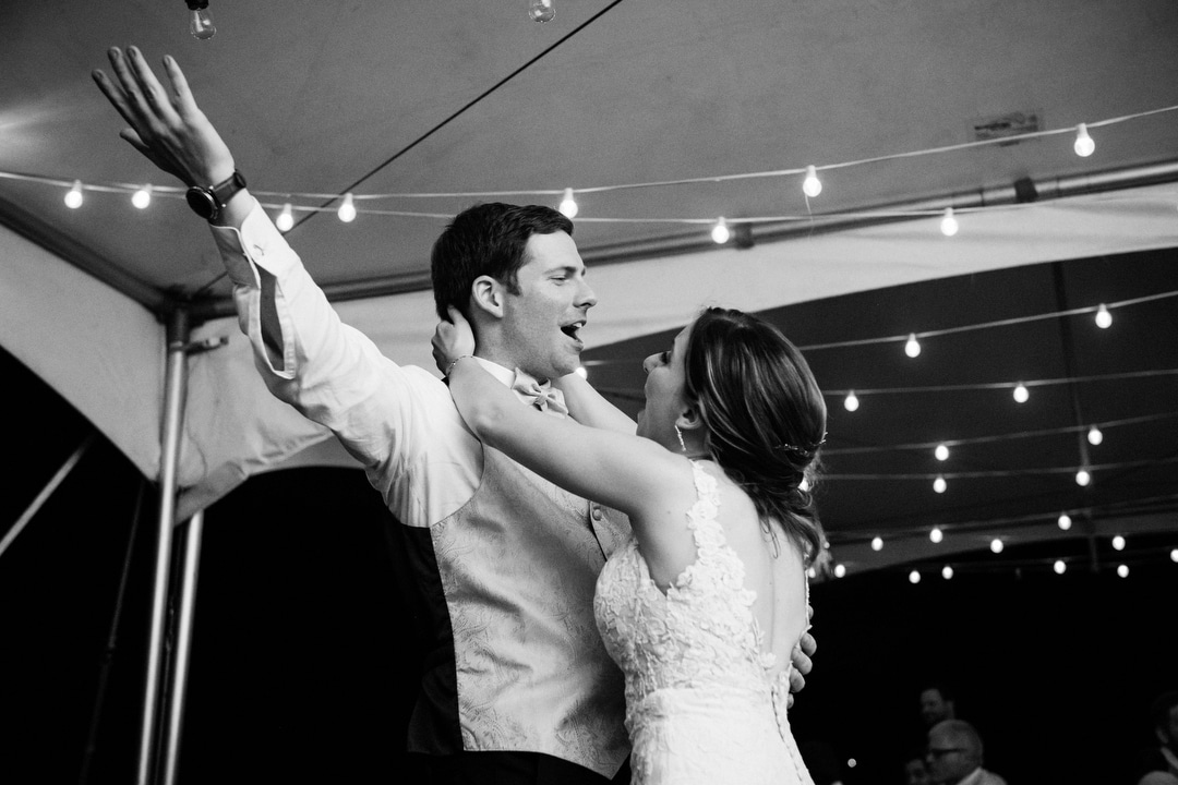 A bride embraces her groom as he sings and holds his hands in the hair during their reception at Gilfillan Farm.