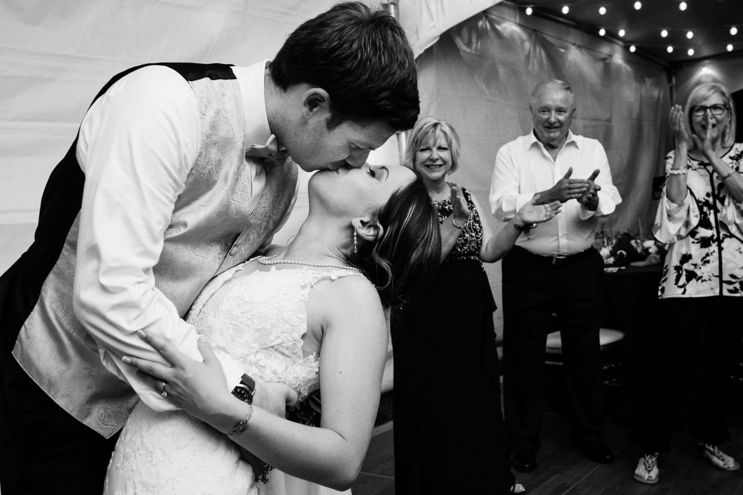 A groom dips his bride and gives her a kiss while their guests applaud.
