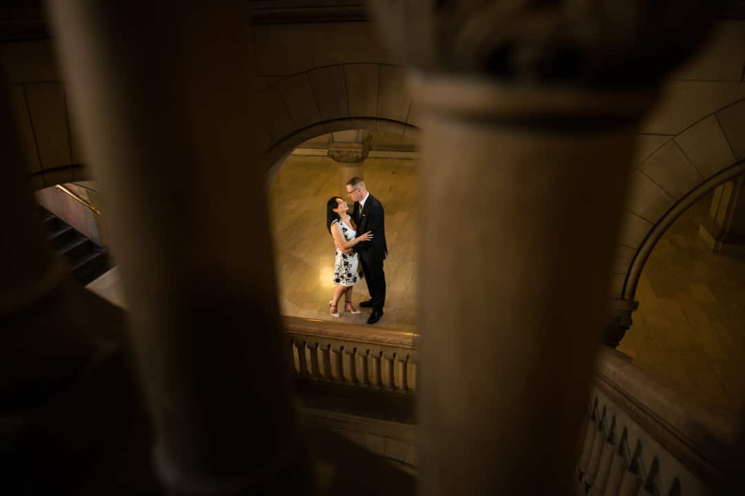 A couple is seen through stone arches as they embrace in the foyer of the Allegheny County Courthouse after their wedding.