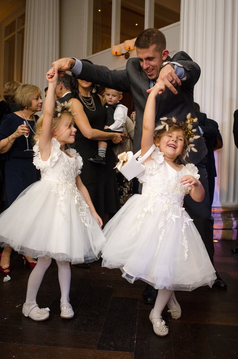 Two flower girls wearing white dresses spin while dancing with their father during a wedding reception at the Hotel Monaco.