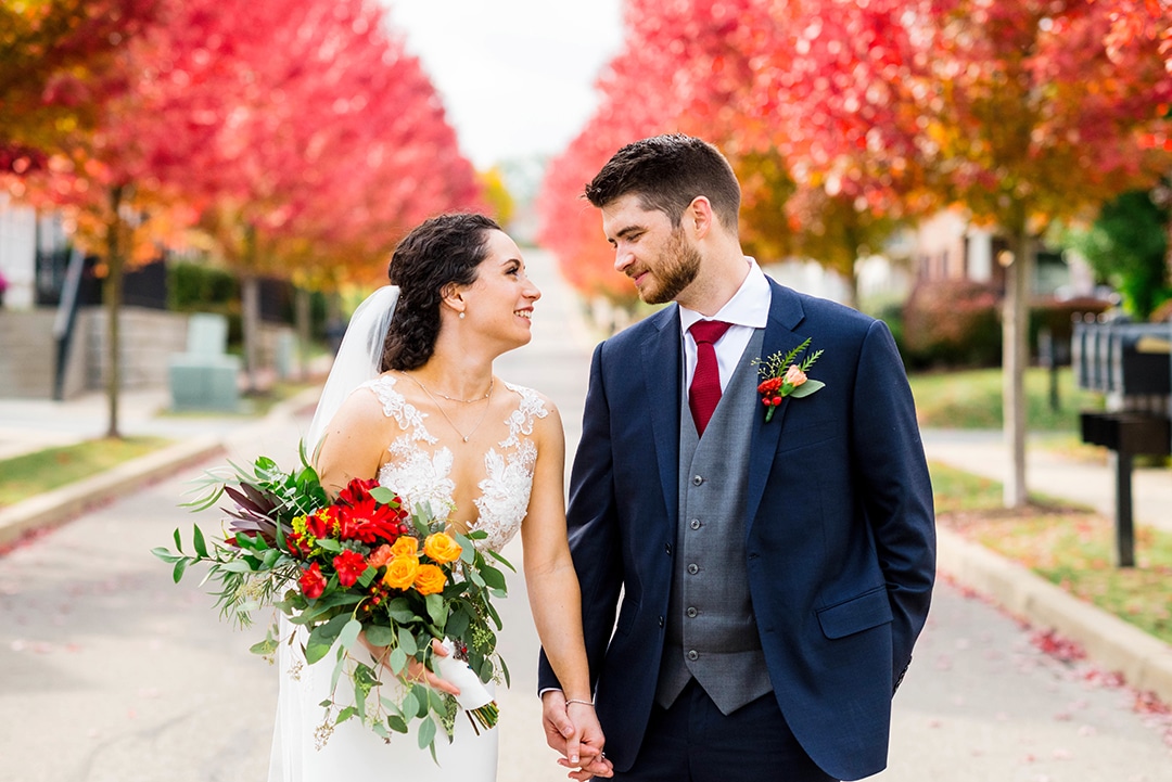 A bride and groom hold hands and look at each other with fall foliage behind them. When your work is among the world's best wedding photos you've got to up your game!