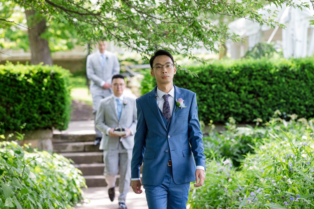 A groom walks towards the outdoor garden at the beginning of his Phipps outdoor wedding.