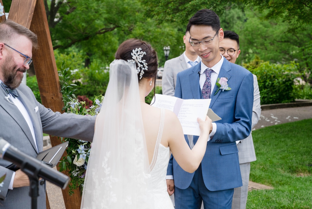 A groom smiles as he reads his vows during a Phipps outdoor wedding.