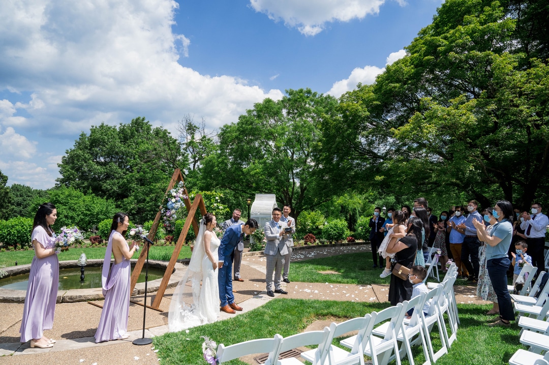 A groom bows as he and his bride face their guests at the end of a Phipps outdoor wedding.
