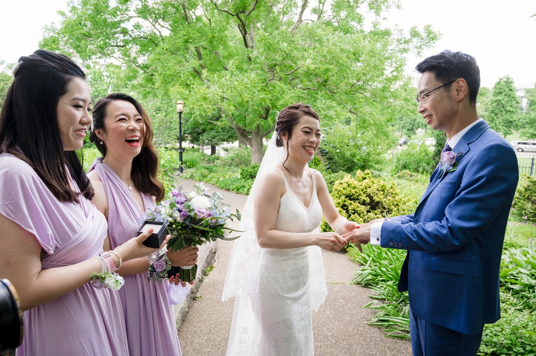 A bride and her bridesmaids laugh as she tries to put a wedding ring on the finger of her groom at Phipps.