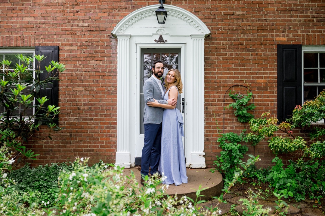 A bride and groom pose for a portrait at the front door of his parent's house at their outdoor intimate wedding.
