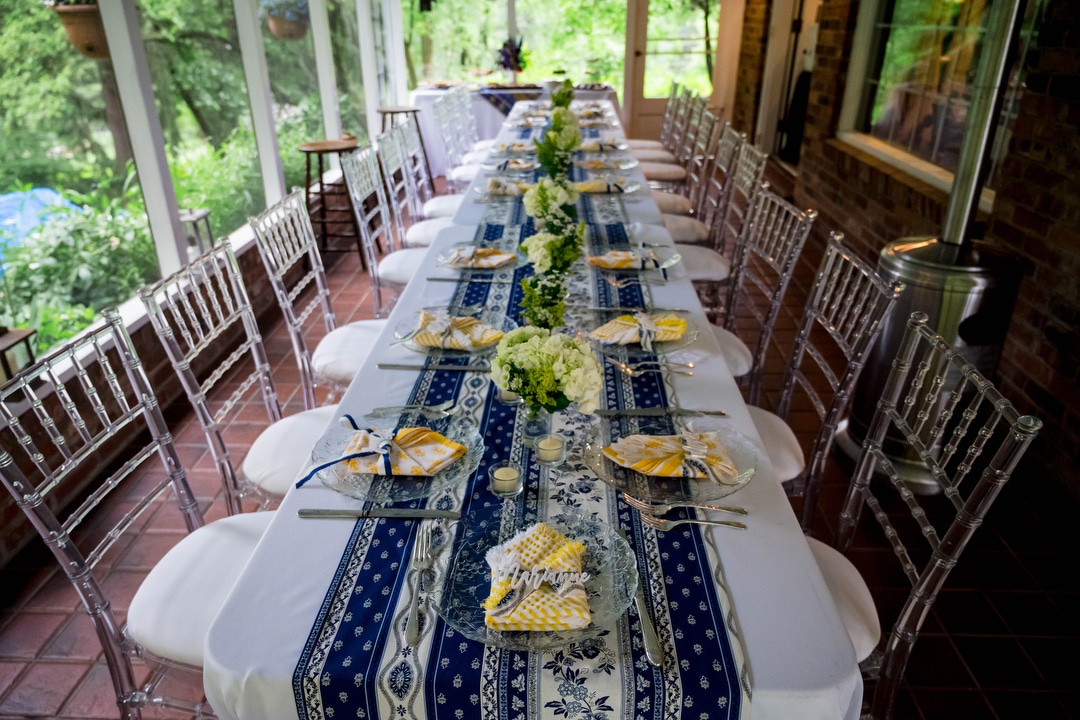 A long dinner table is set up in a screened porch.