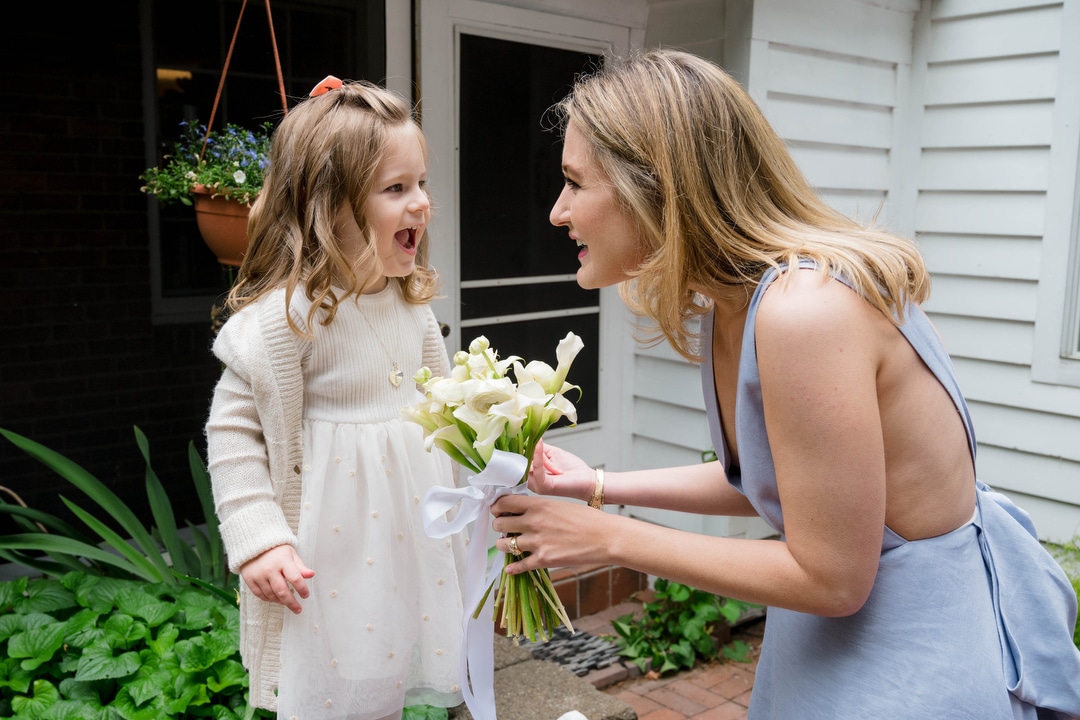 A bride in a blue dress smiles as she shows a small girl her bouquet.