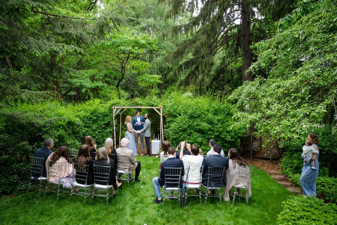 An outdoor intimate wedding ceremony takes place under a chuppah.