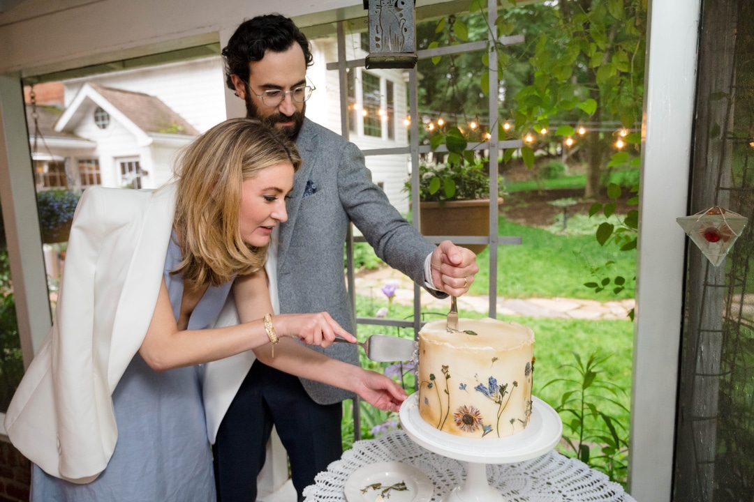 A bride and groom cut their cake on the screened back porch of the groom's parent's house.