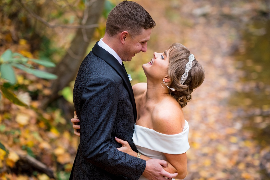 a bride and groom embrace while standing on a bed of fallen leaves