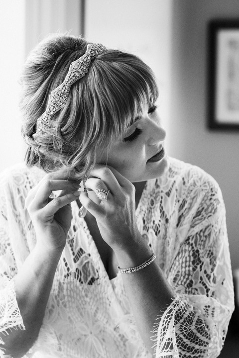black and white image of a woman putting on earrings.