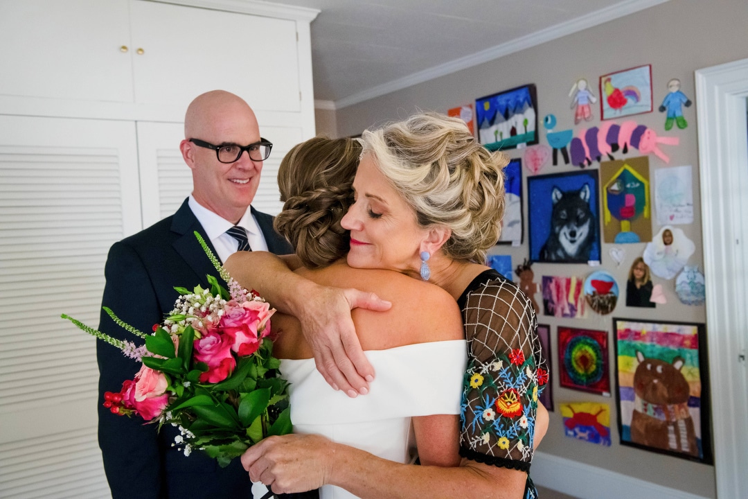 A mother hugs her daughter while her father looks on before a wedding.