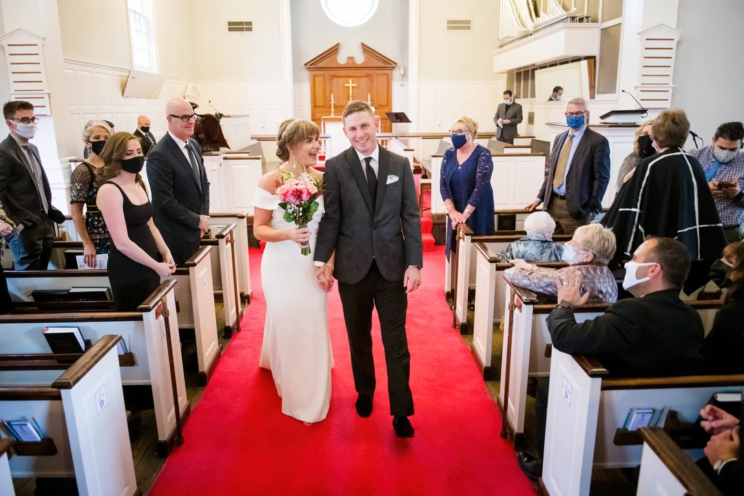 A bride and groom walk down the red carpeted aisle of a church at the end of their wedding.