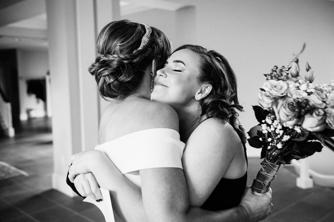 A bride's sister gives her a hug after her wedding.