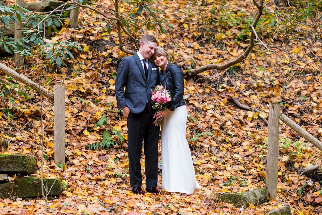 A bride and groom stand together in a leaf-covered forest.