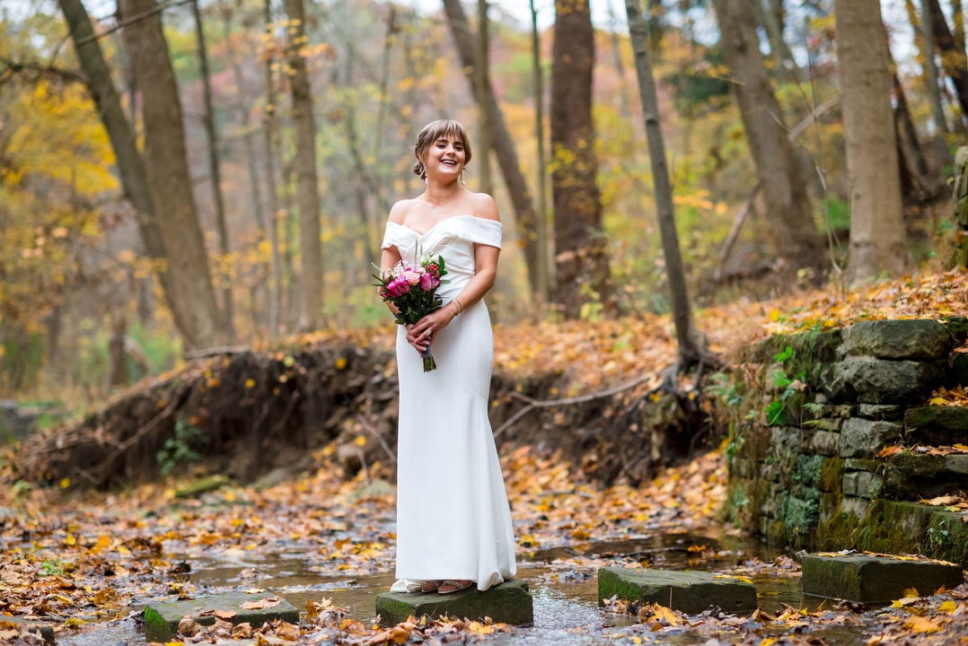 A bride poses for a portrait on a stepping stone in a forest stream.