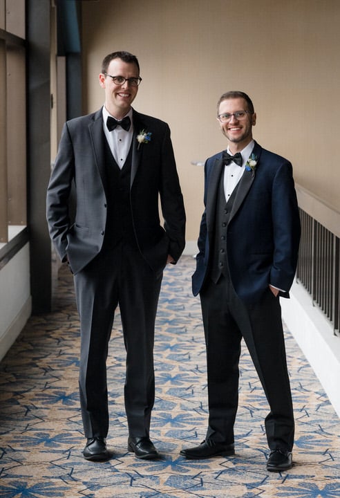 A tall groom and a shorter groom stand together for a portrait at the Sheraton Station Square.