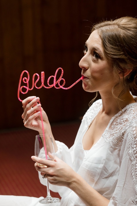 A young woman drinks champagne through a straw shaped into the word "Bride"