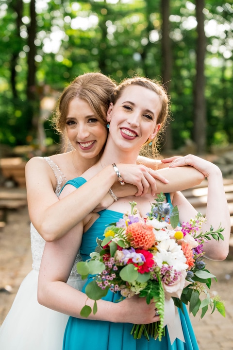 a bride embraces her sister who holds a bouquet of flowers.