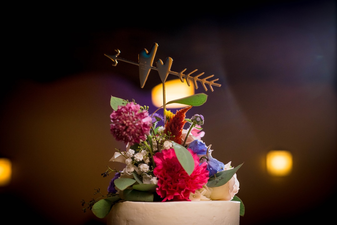 Detail of the top of a wedding cake with flowers and hearts run through by an arrow.