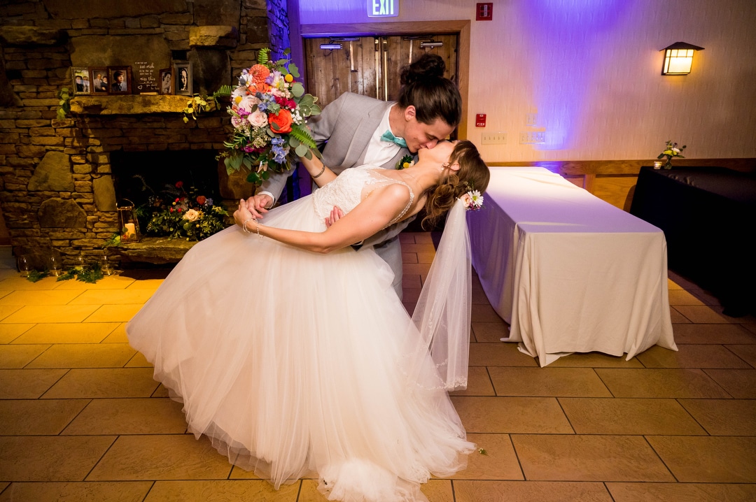 A groom dips his bride and kisses her as they enter their wedding reception.