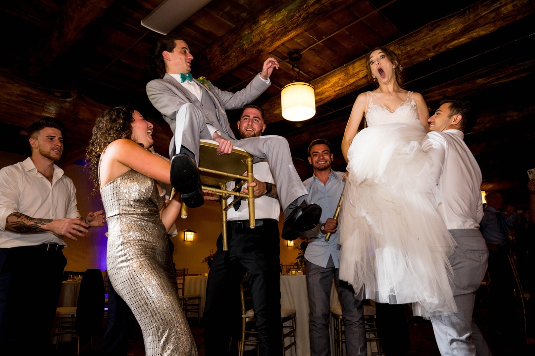 A bride and groom are raised on chairs during the hora at their summer wedding at seven springs.