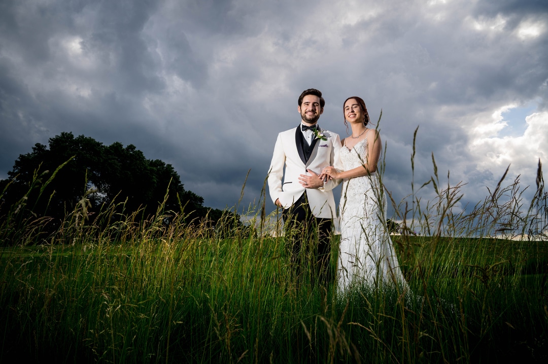 With a dramatic, stormy sky in the background, a couple poses for a photo after their wedding at Oakmont Country club.