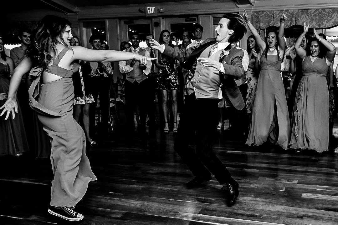A woman and a man jump in the air while dancing at a wedding reception at Oakmont country club.