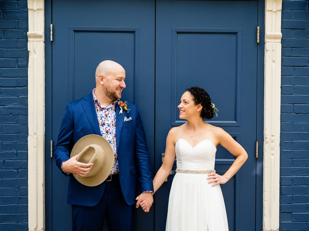 Bride and groom hold hands and look at each other in front of a set of blue doors at the Hotel Indigo in Pittsburgh.