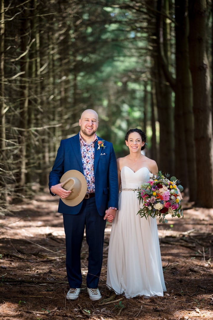 A bride and groom hold hands while standing in a grove of pine trees before their Gardens of Stonebridge Wedding.