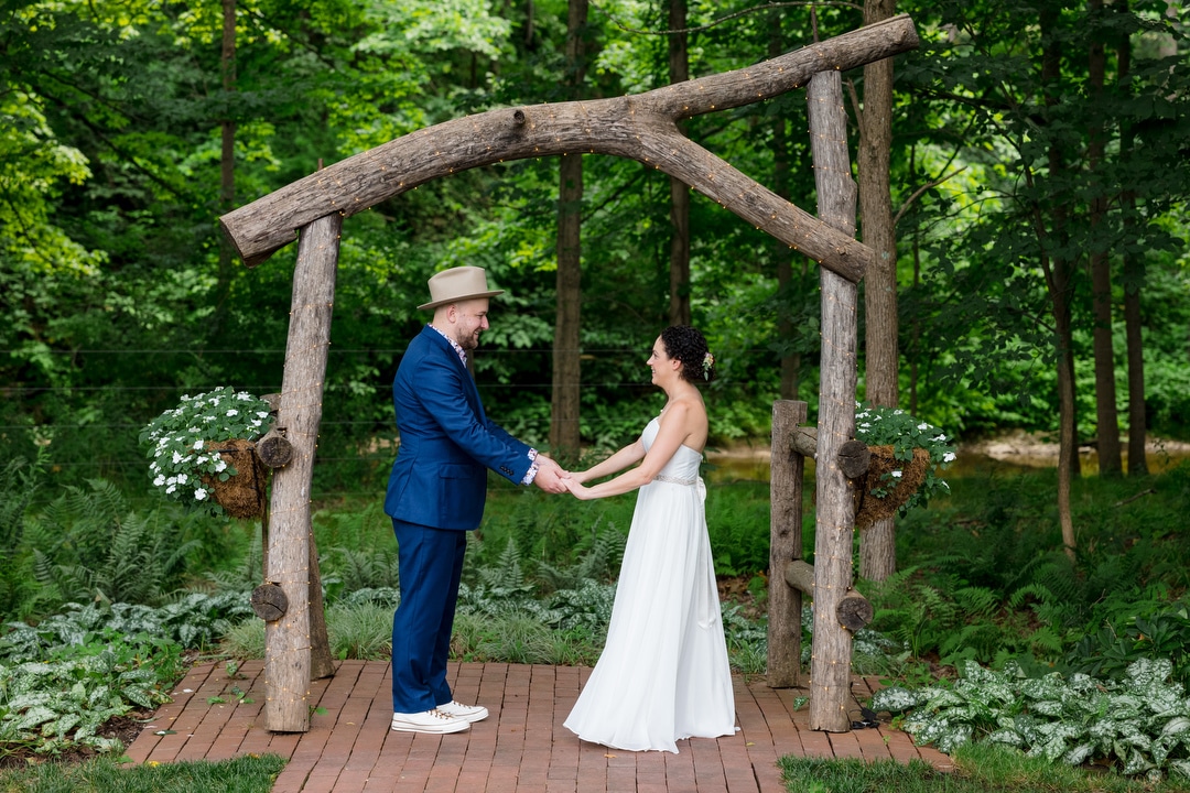 A couple hold hands beneath a wooden arch before their Gardens of Stonebridge Wedding.