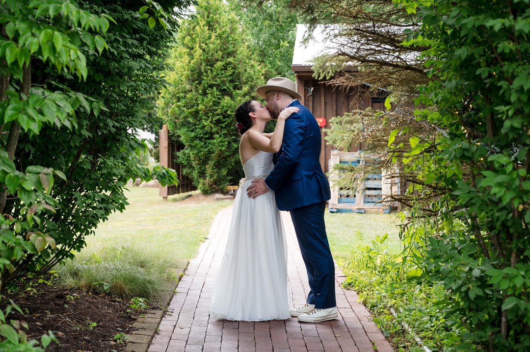 A couple kisses along a brick path during their Gardens of Stonebridge Wedding.