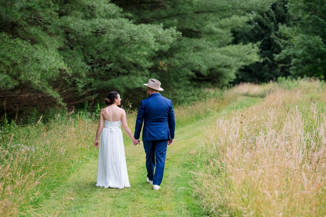 A bride and groom walk along a grassy path during their Gardens of Stonebridge Wedding.