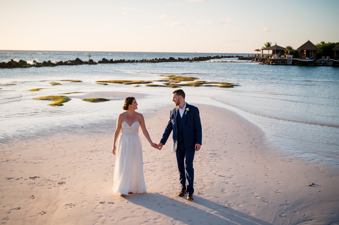 A bride and groom walk on a beach after their destination wedding in Aruba.