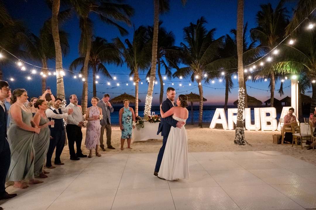 A couple has their first dance under palm trees and bistro lights during their destination wedding in Aruba.