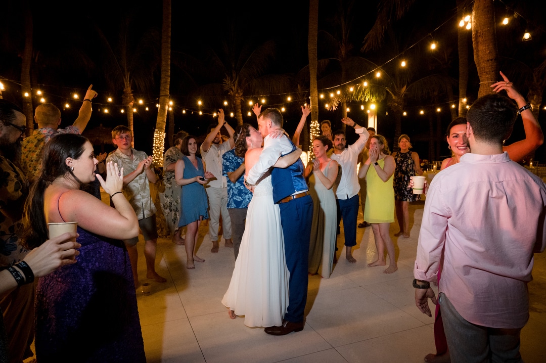 A newlywed couple kisses on the dance floor as their guests surround them during their destination wedding in Aruba.