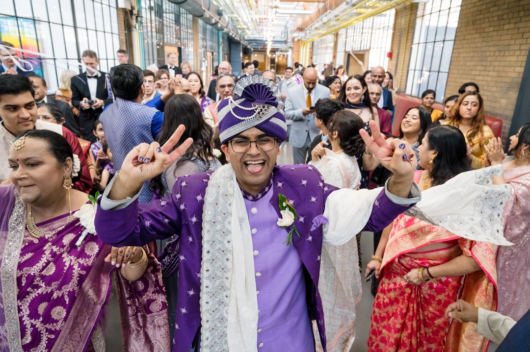A groom in purple South Asian garb leads a group of guests to his wedding at the Energy Innovation Center in Pittsburgh.