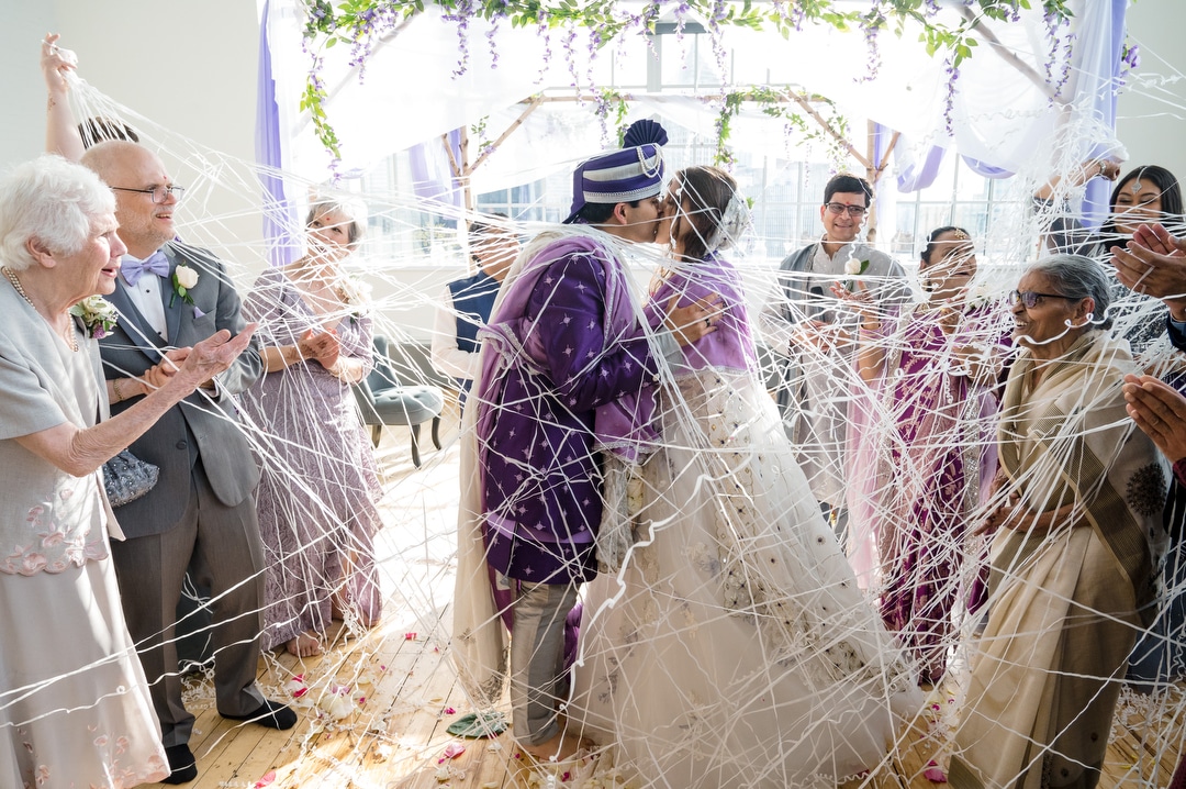 A couple is covered with paper streamers as they kiss at the end of their Energy Innovation Center wedding.
