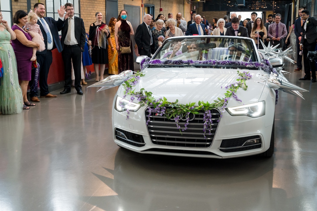 A couple drives an Audi convertible down the corridor as their guests wave after their Energy Innovation Center wedding.
