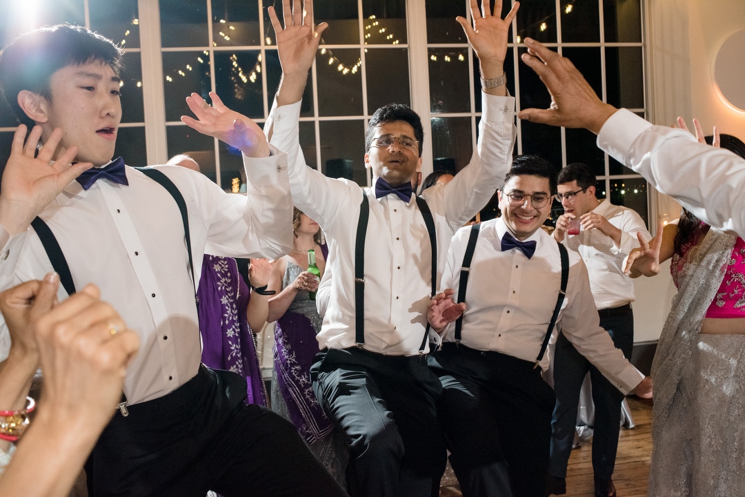 Groomsmen wearing suspenders and white shirts dance during an Energy Innovation Center wedding.