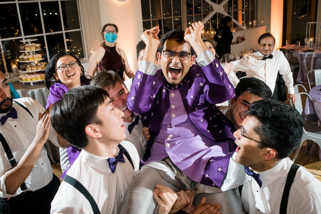 A groom wearing purple is lifted into the air during his wedding at the Energy Innovation Center.