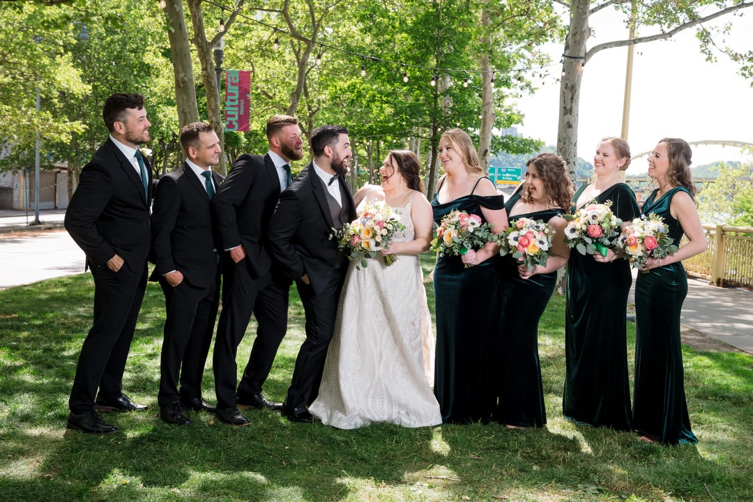 A wedding party shares a laugh outside on a light and airy spring day.