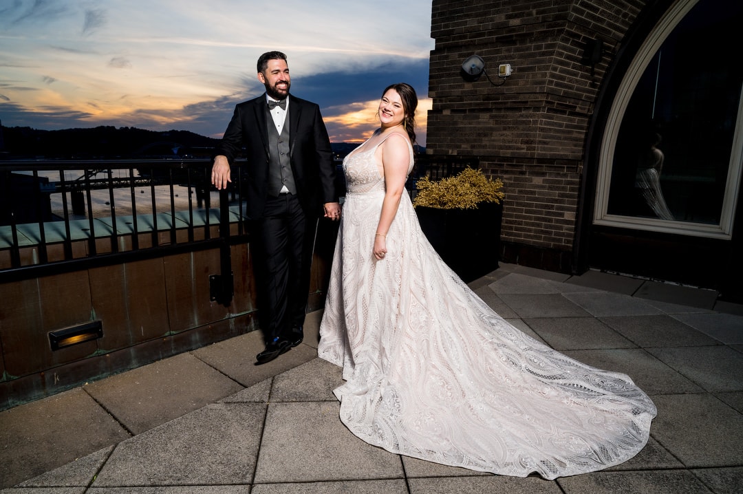 A bride and groom hold hands as they stand on the balcony of their suite at the Renaissance hotel at sunset.